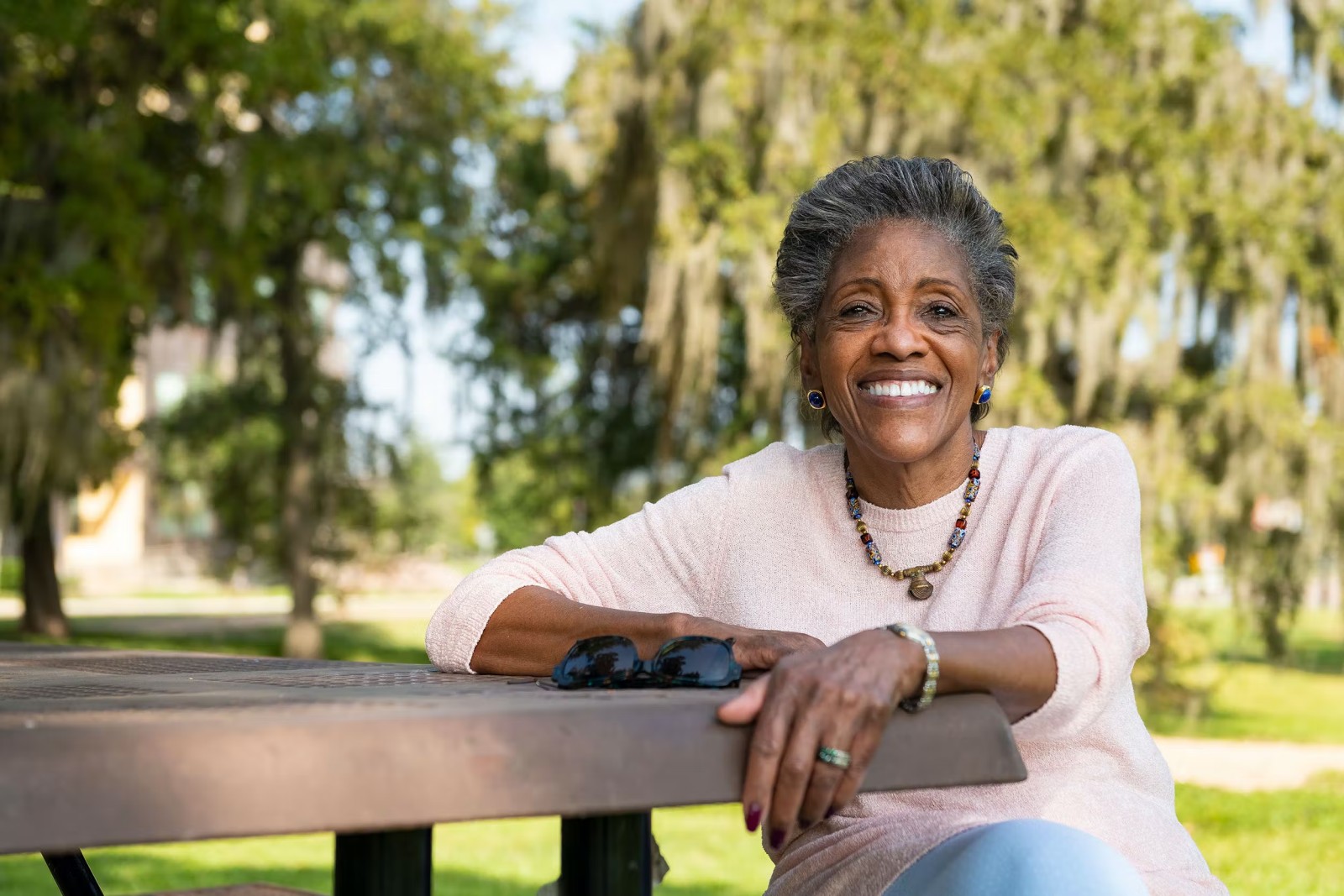 Elderly lady sitting on a bench, surrounded by nature and smiling